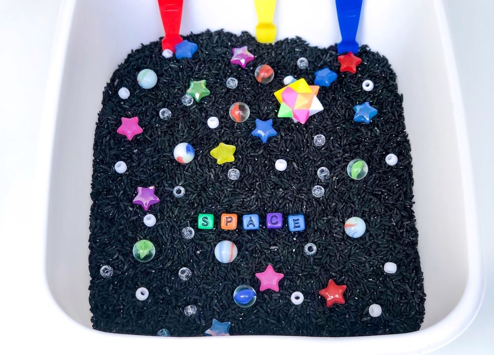 outer space sensory bin with black rice, marbles, and stars